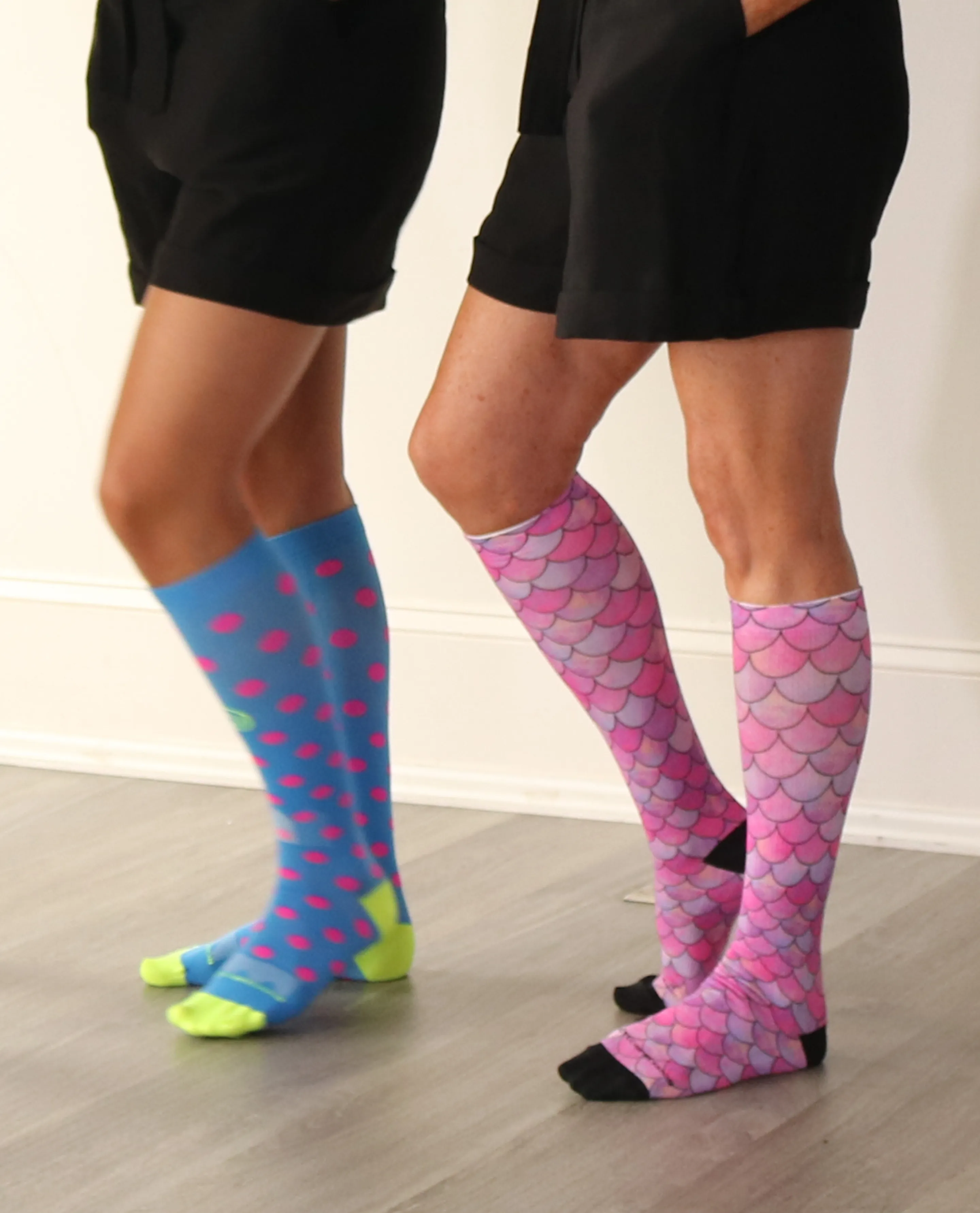 The lower legs of three people wearing black shorts and different pairs of colorful, patterned knee-high socks.
