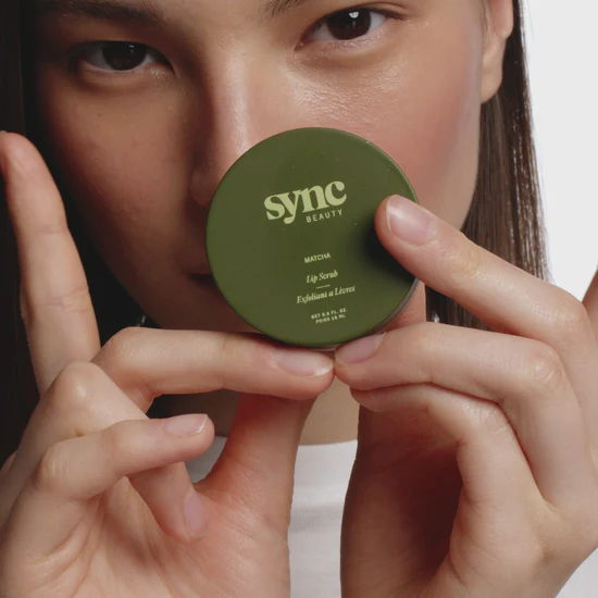 Person applying green lip scrub, smiling.