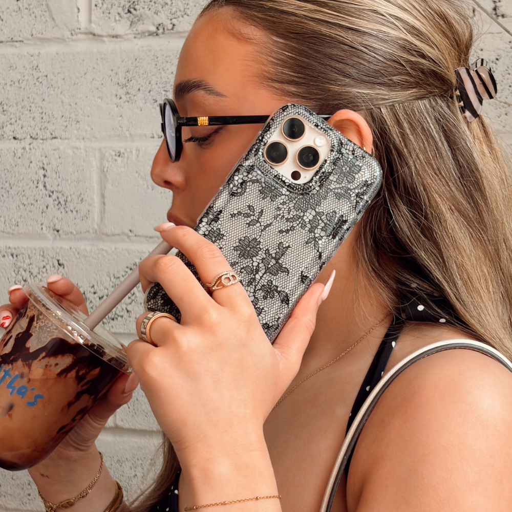 Two floral phone cases on a magazine cover next to a pink bag and a red drink.