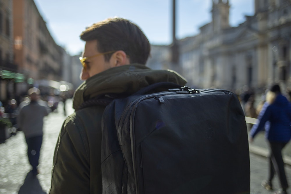 Person with a backpack walking in a sunny urban street.