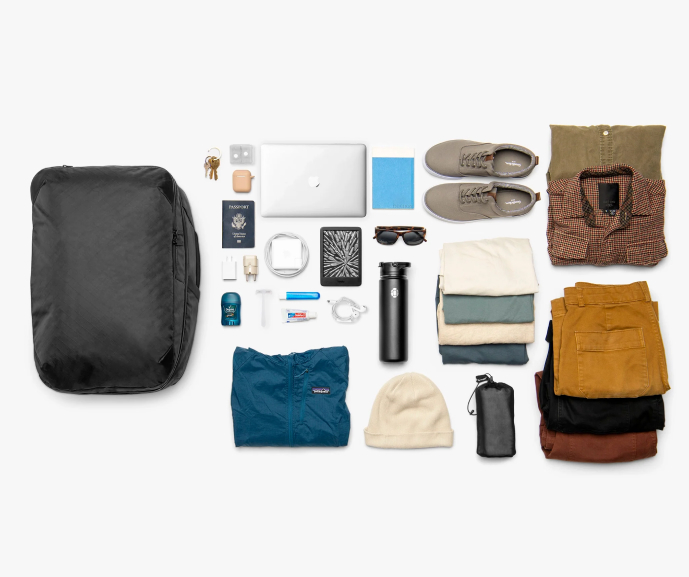 Travel essentials neatly arranged, including clothes, shoes, a backpack, and electronic devices.