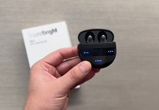 Hand holding wireless earbuds with charging case, product box in background.