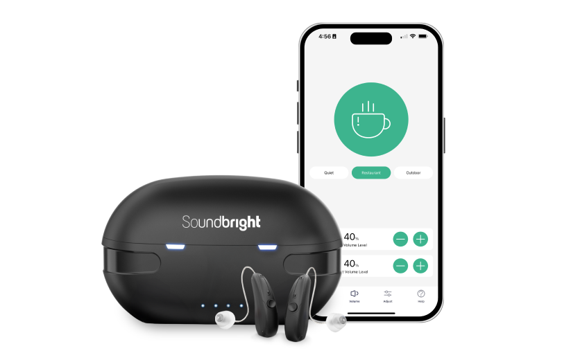 A person holds a small, black behind-the-ear hearing aid between their thumb and forefinger with a blurred green background.