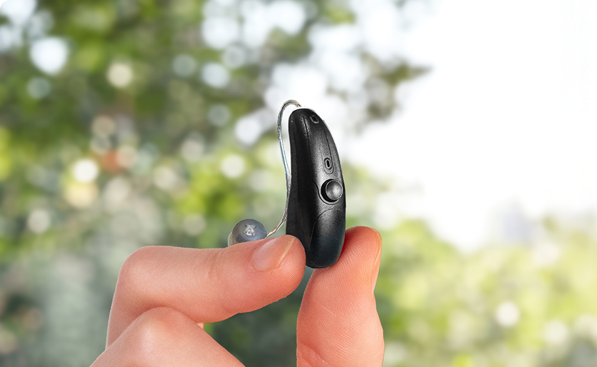A pair of Soundbright hearing aids sit in front of their black, circular charging case.