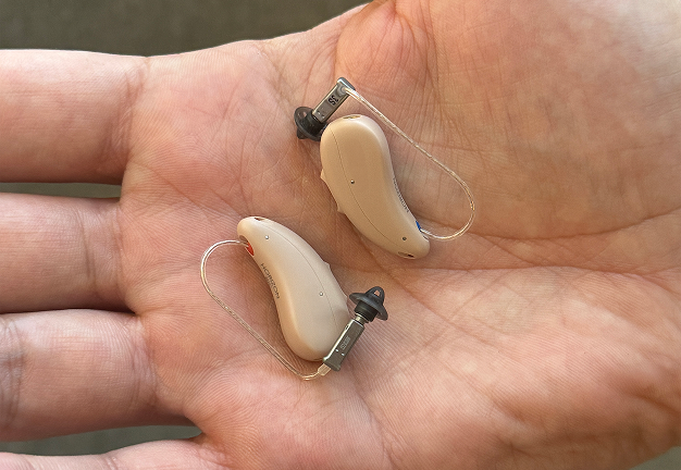 A close-up of two beige hearing aids resting on the palm of a hand.