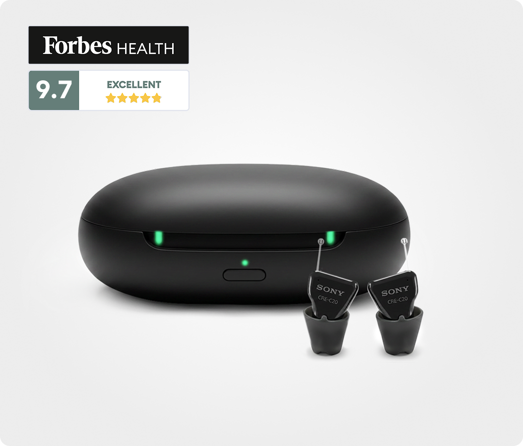 A pair of black Sony CRE-C20 hearing aids in front of their charging case, with a Forbes Health rating.