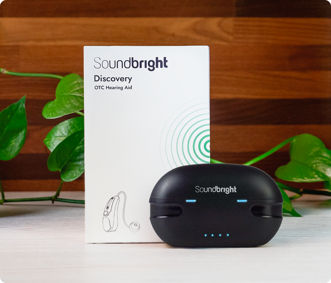 Soundbright hearing aid box and black case on wooden surface with green plant.