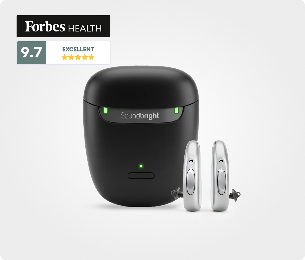 A pair of silver Soundbright hearing aids next to their black charging case, with a Forbes Health rating.