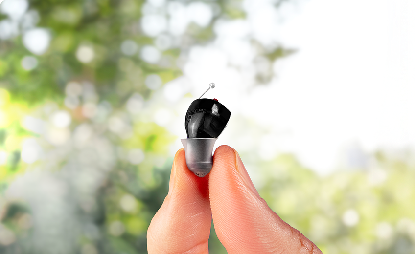 A pair of Soundbright hearing aids sit in front of their black, circular charging case.