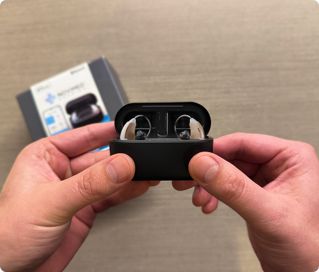 Hands holding a black case with two hearing aids inside.