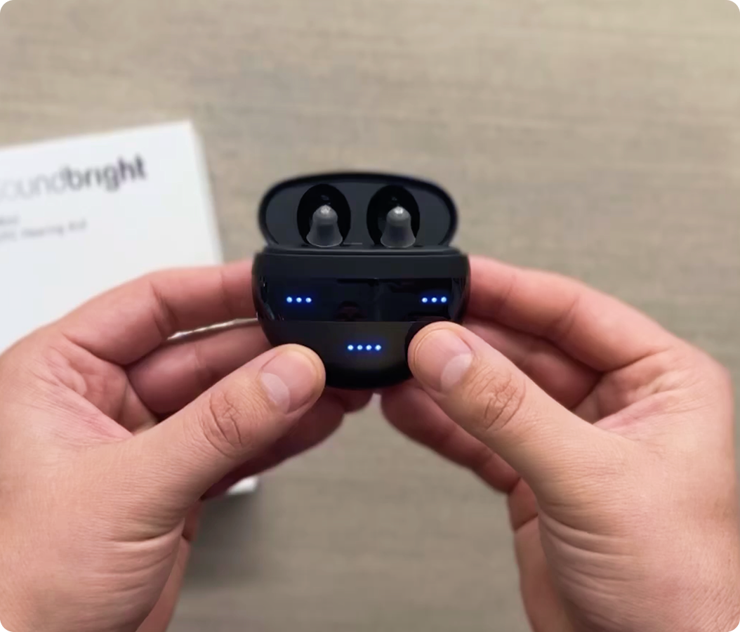 Hands holding black earbuds with glowing blue lights on the case.