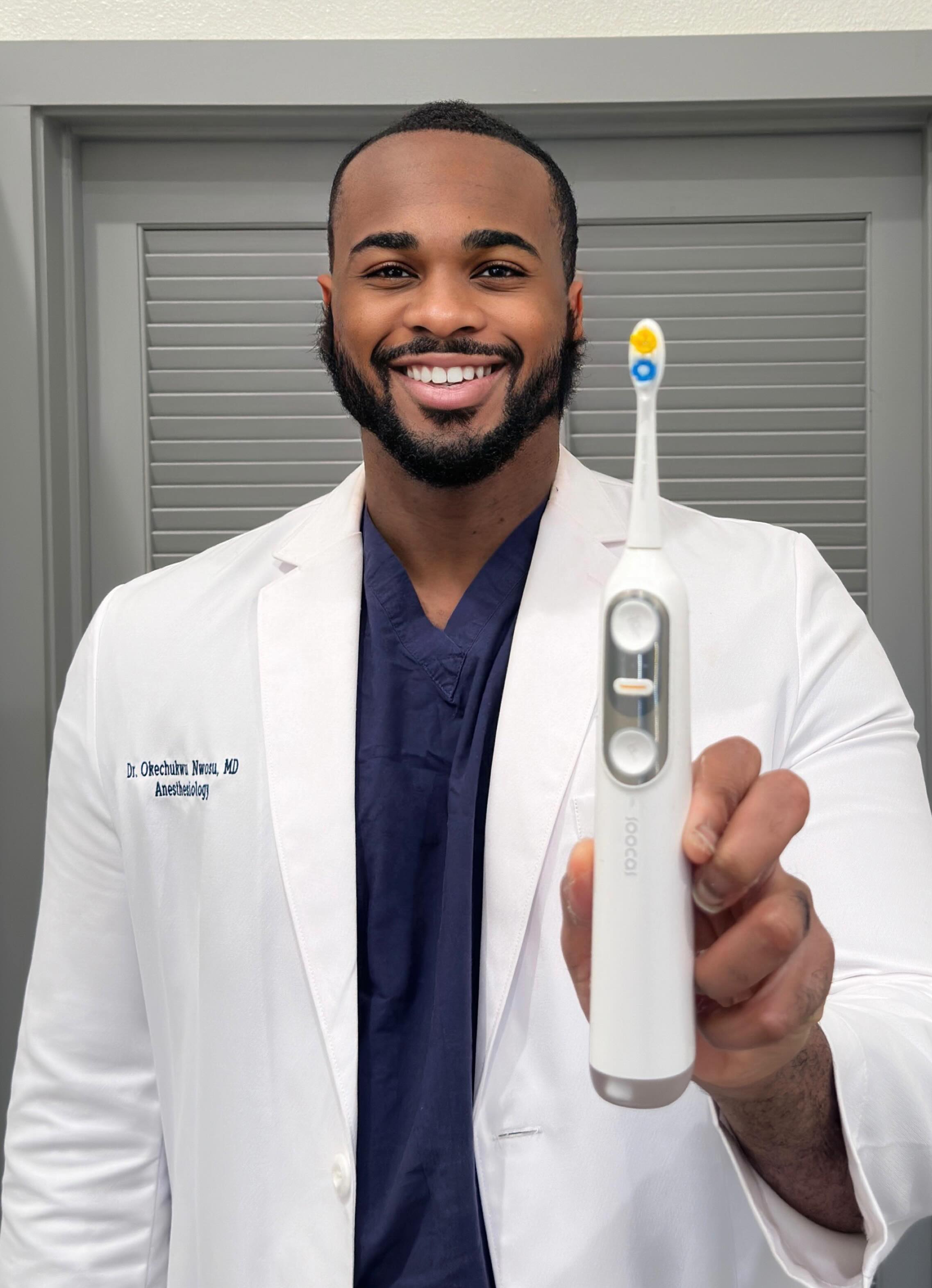 Person in a white coat holding an electric toothbrush.