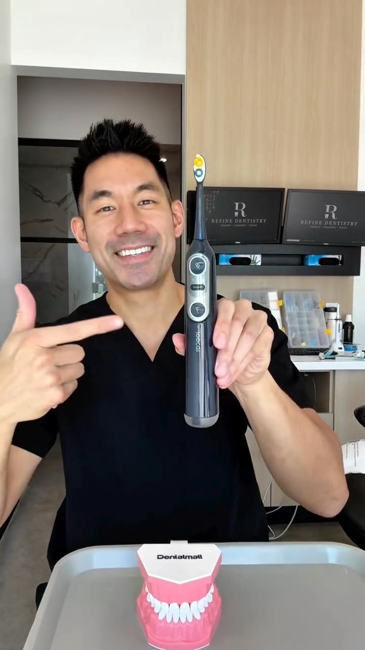Person holding an electric toothbrush and pointing at it, with dental model on tray.