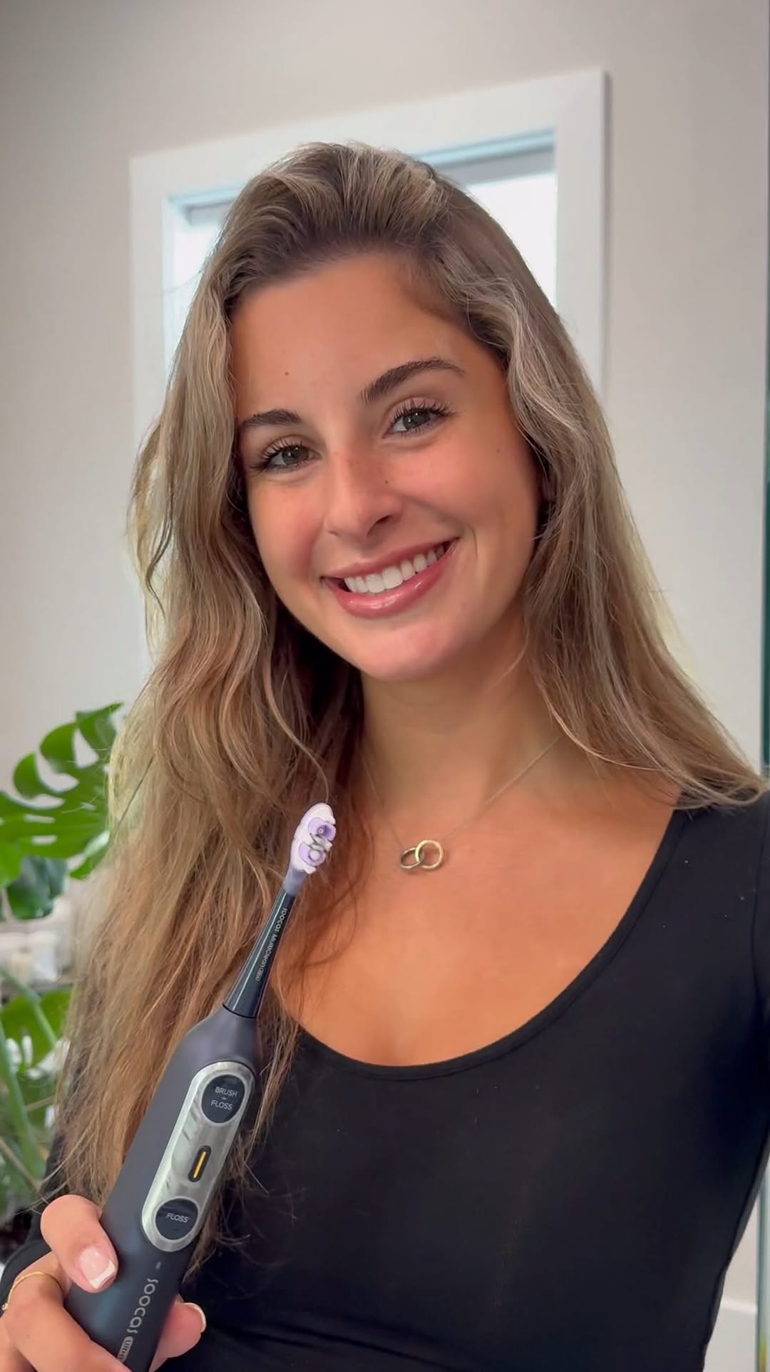 Smiling person holding a black electric toothbrush indoors.