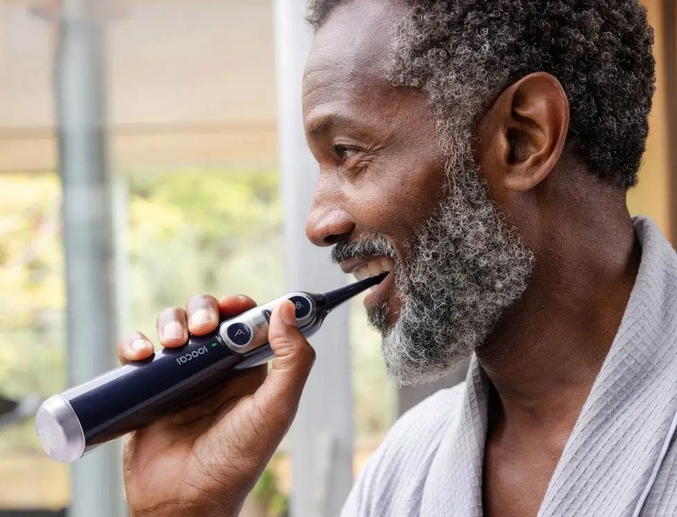 Person using an electric toothbrush in a bathroom setting.