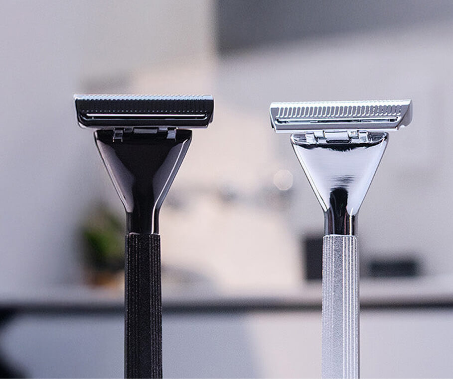 Two safety razors, one black and one silver, on a blurred background.