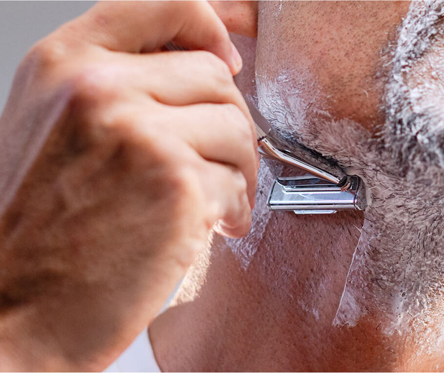 Close-up of a person shaving with a razor and shaving cream.