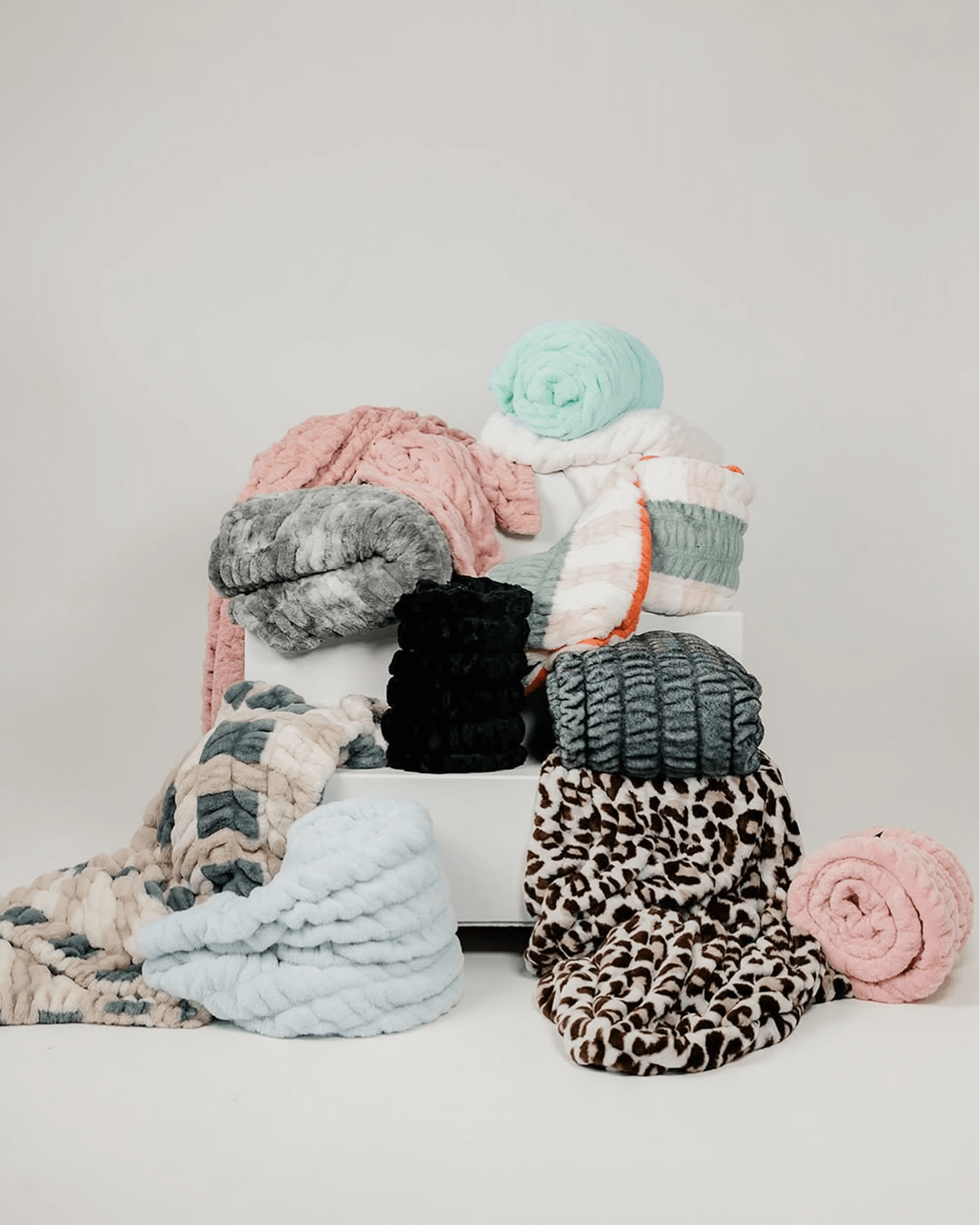 A variety of colorful, textured blankets stacked and draped on a white surface.