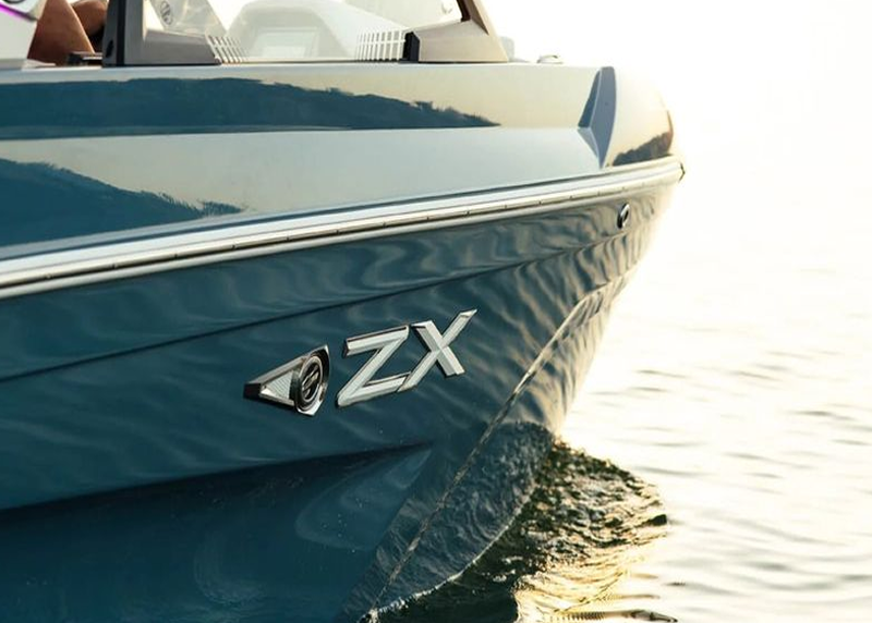 A close-up of the side of a teal boat with a chrome 'ZX' logo, floating on the water.