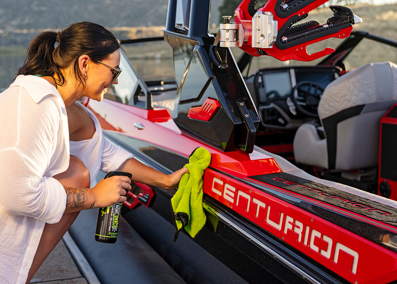 A woman smiles as she wipes down the side of a red Centurion boat with a cloth.