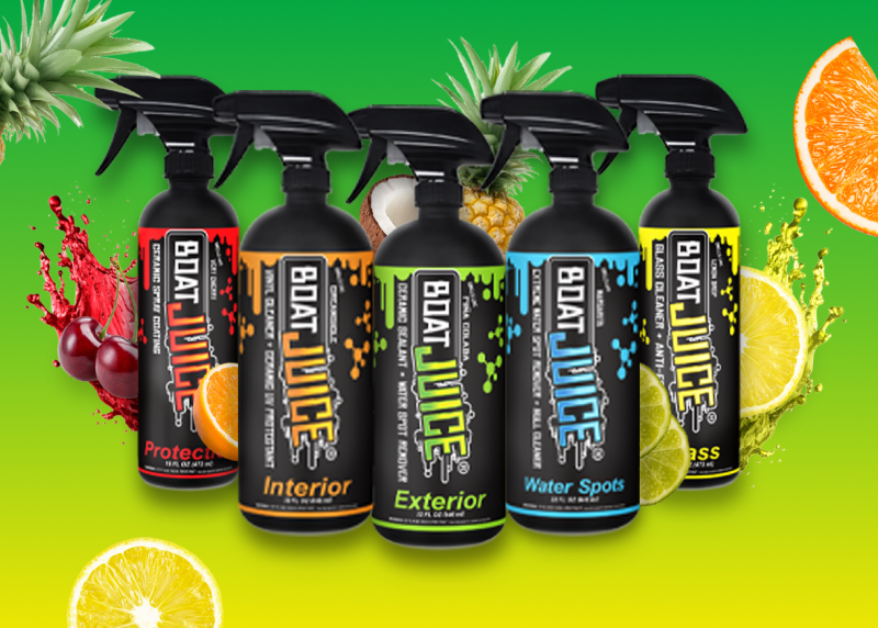 A lineup of five Boat Juice cleaning spray bottles arranged on a green background with various fruits.