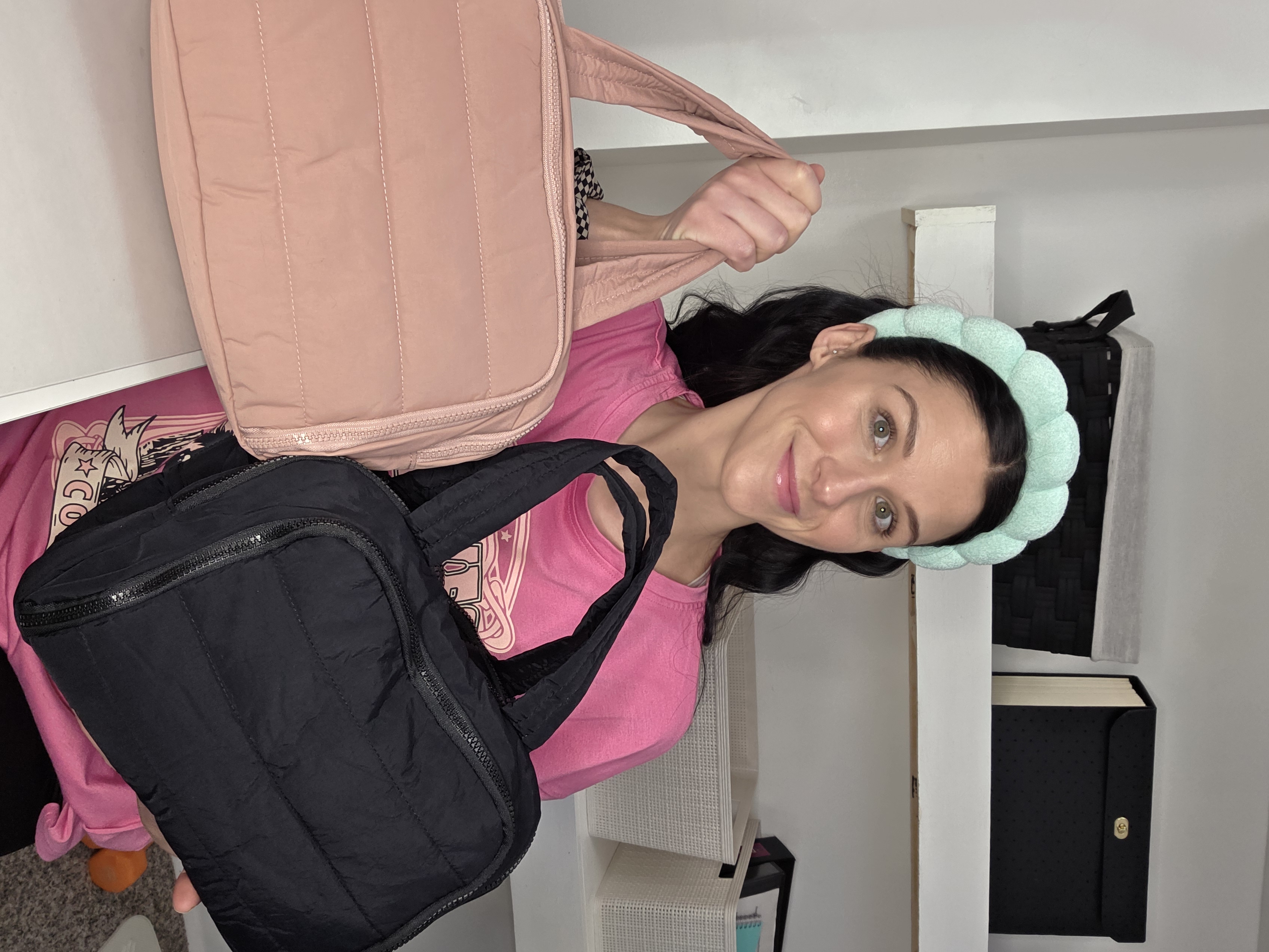 A woman with a puffy green headband holds up a pink quilted bag and a black quilted bag.