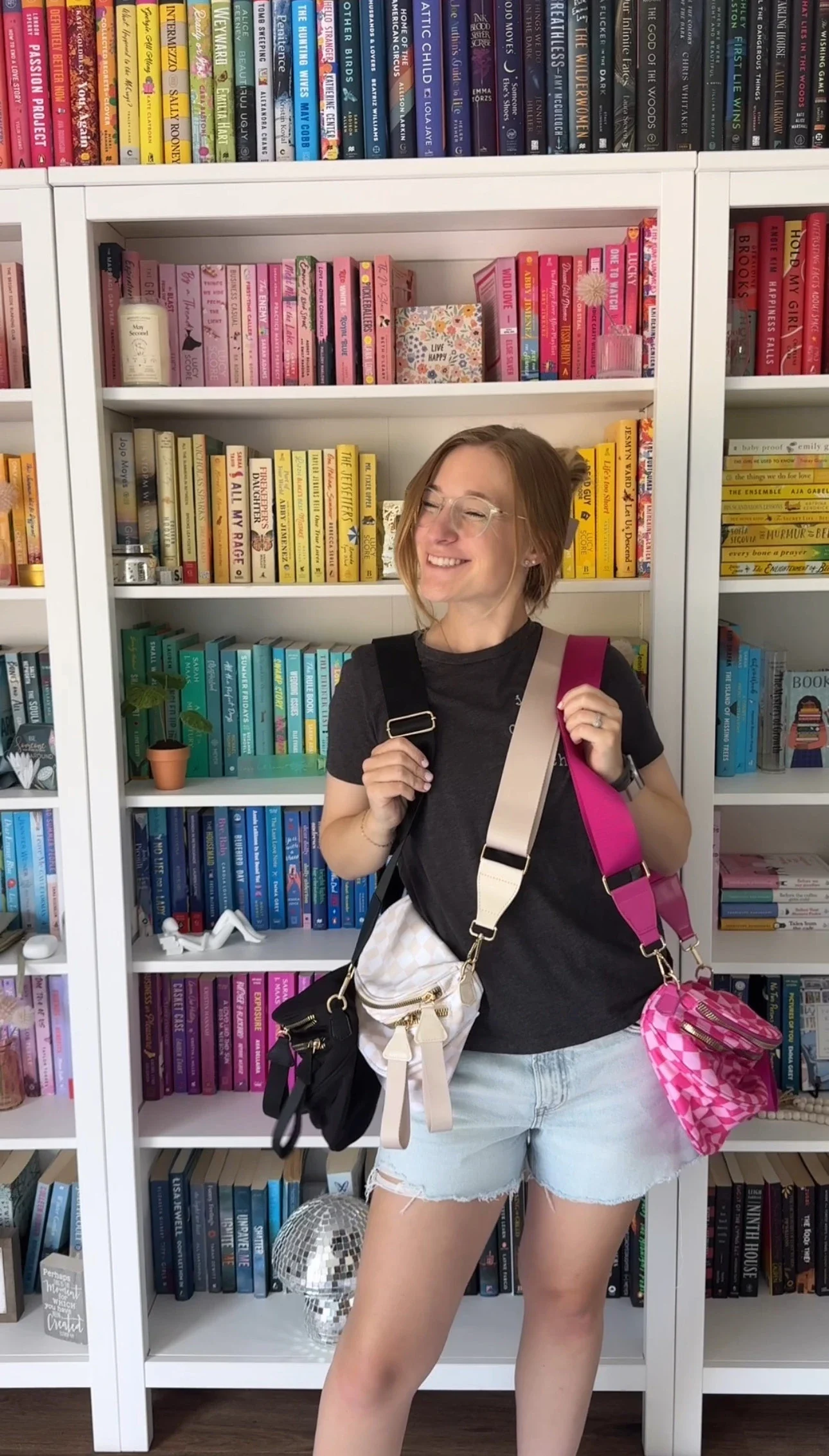 Person smiling with multiple bags in front of colorful bookshelves.