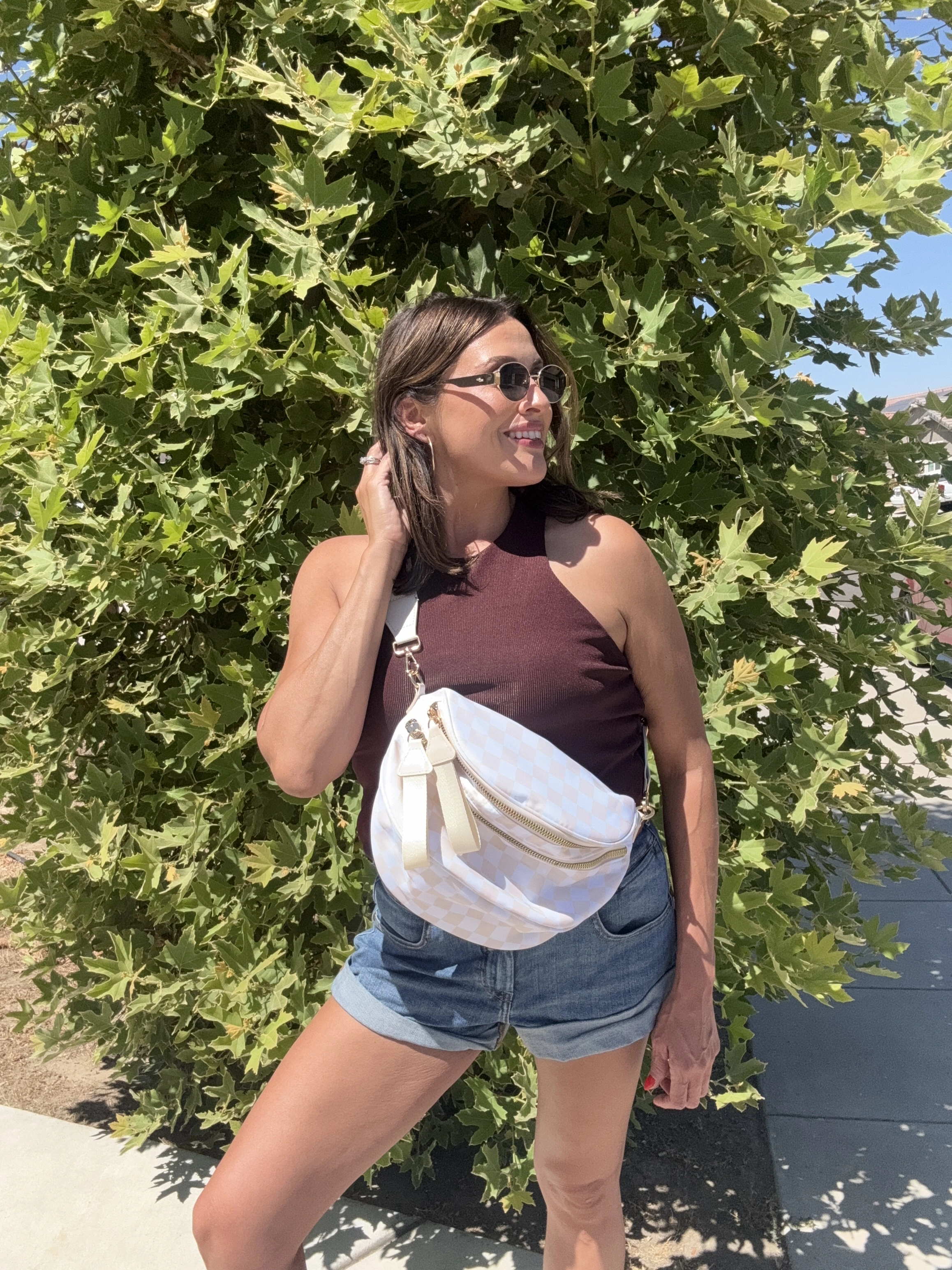 Person in sunglasses and casual outfit standing in front of a leafy tree.
