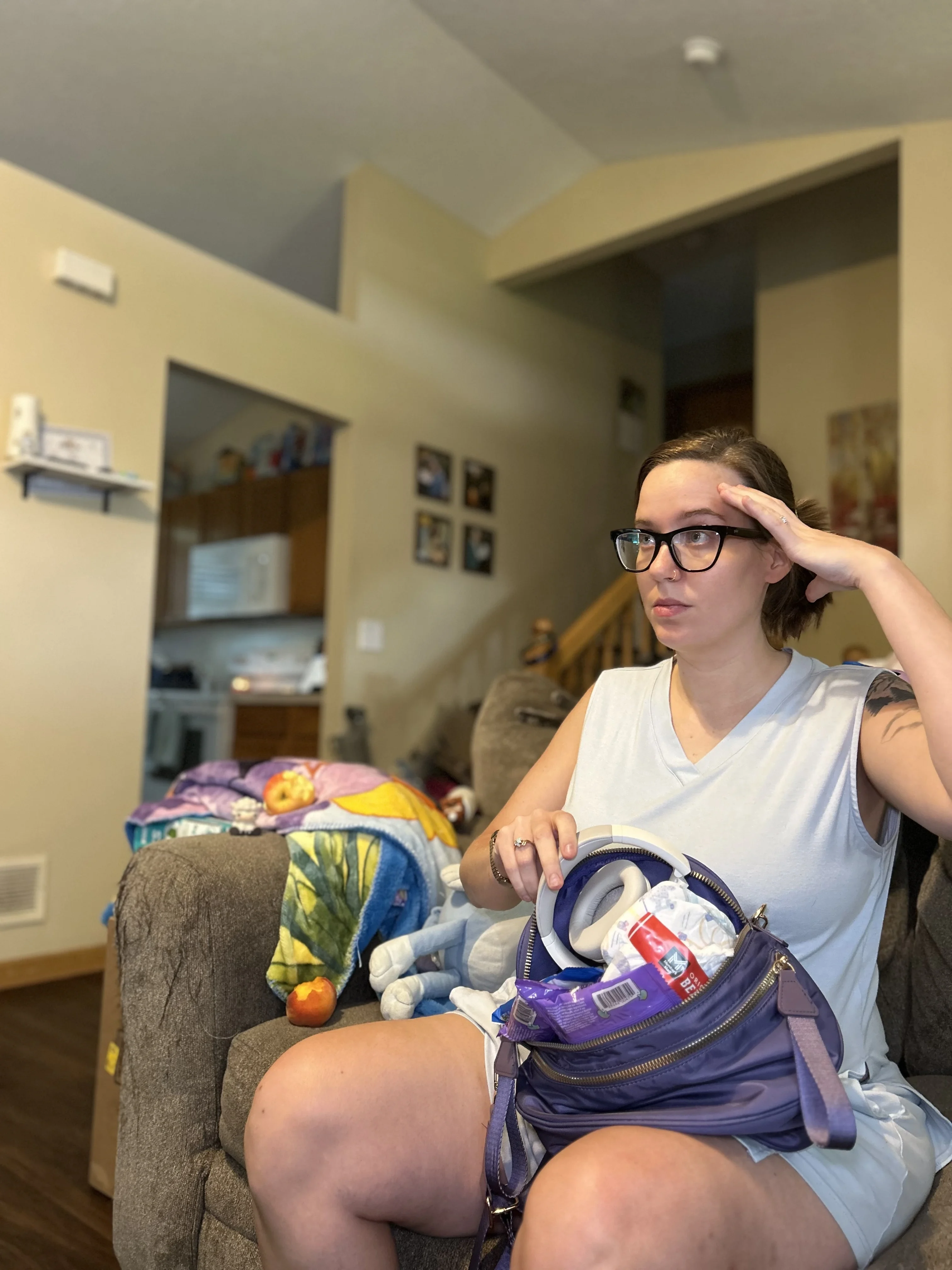 Person sitting on a couch with a purple bag, surrounded by household items.