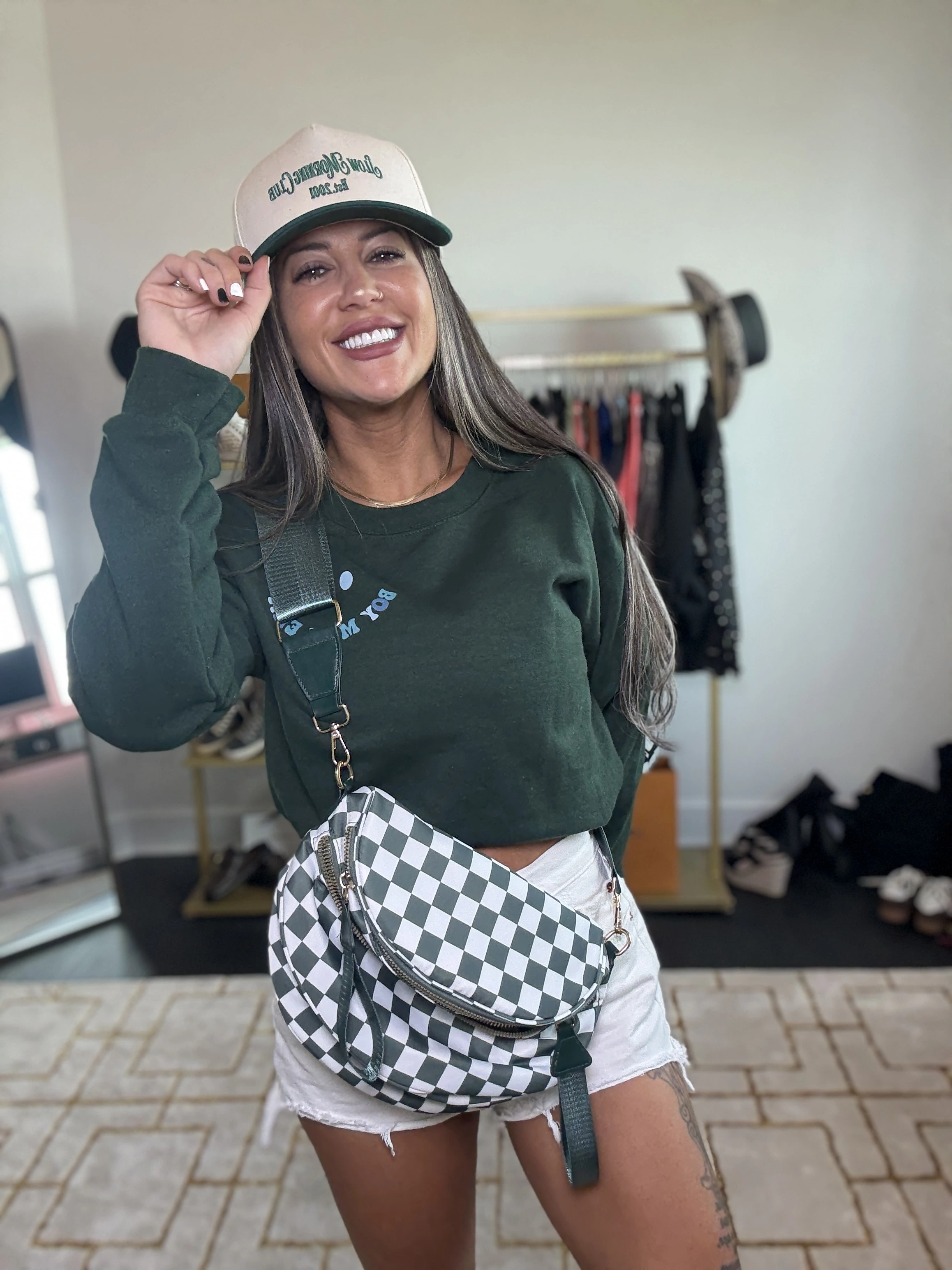 Smiling woman in a green sweater and cap, holding a checkered bag.