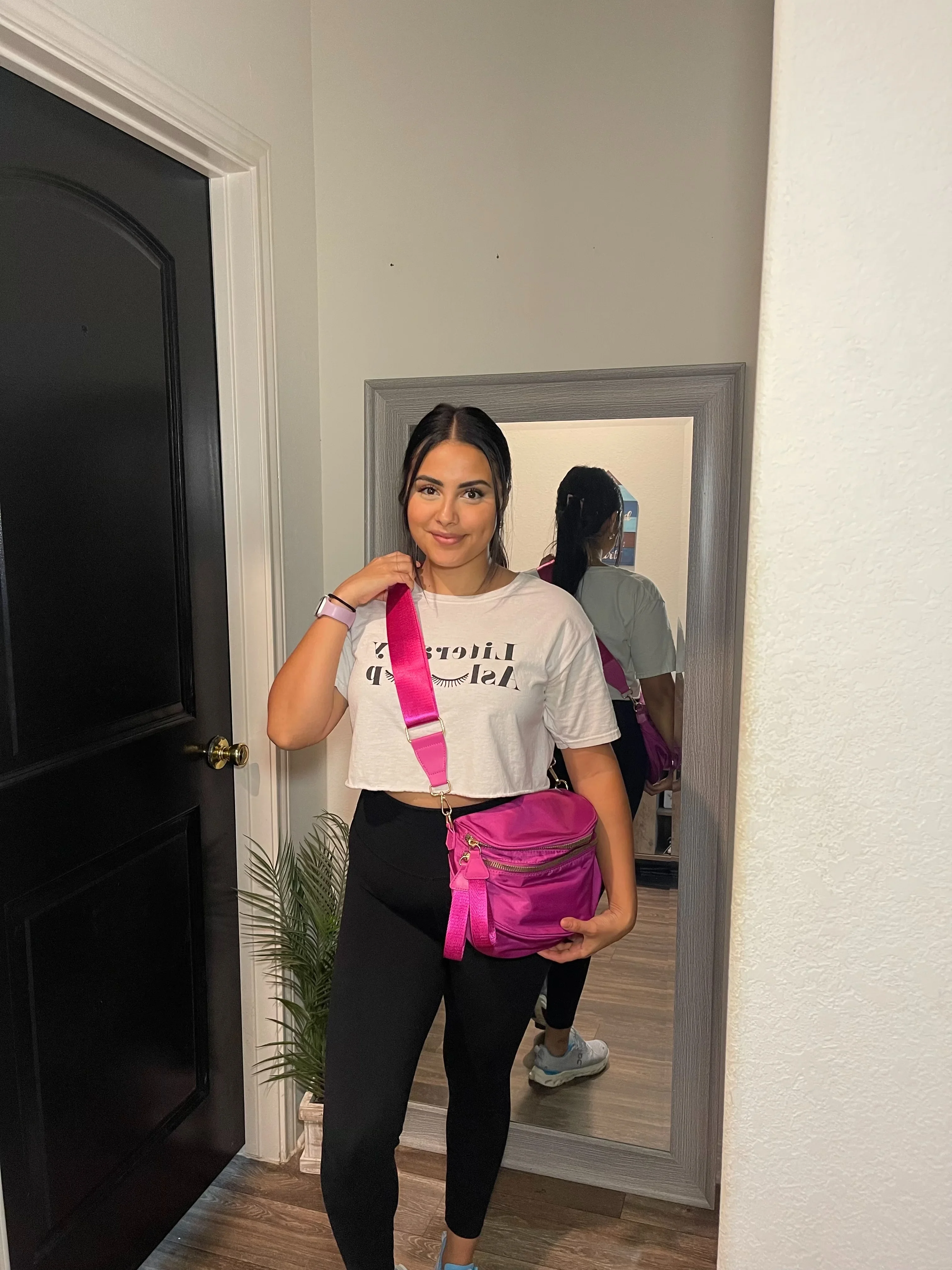 Person standing with a pink bag, reflected in a mirror.