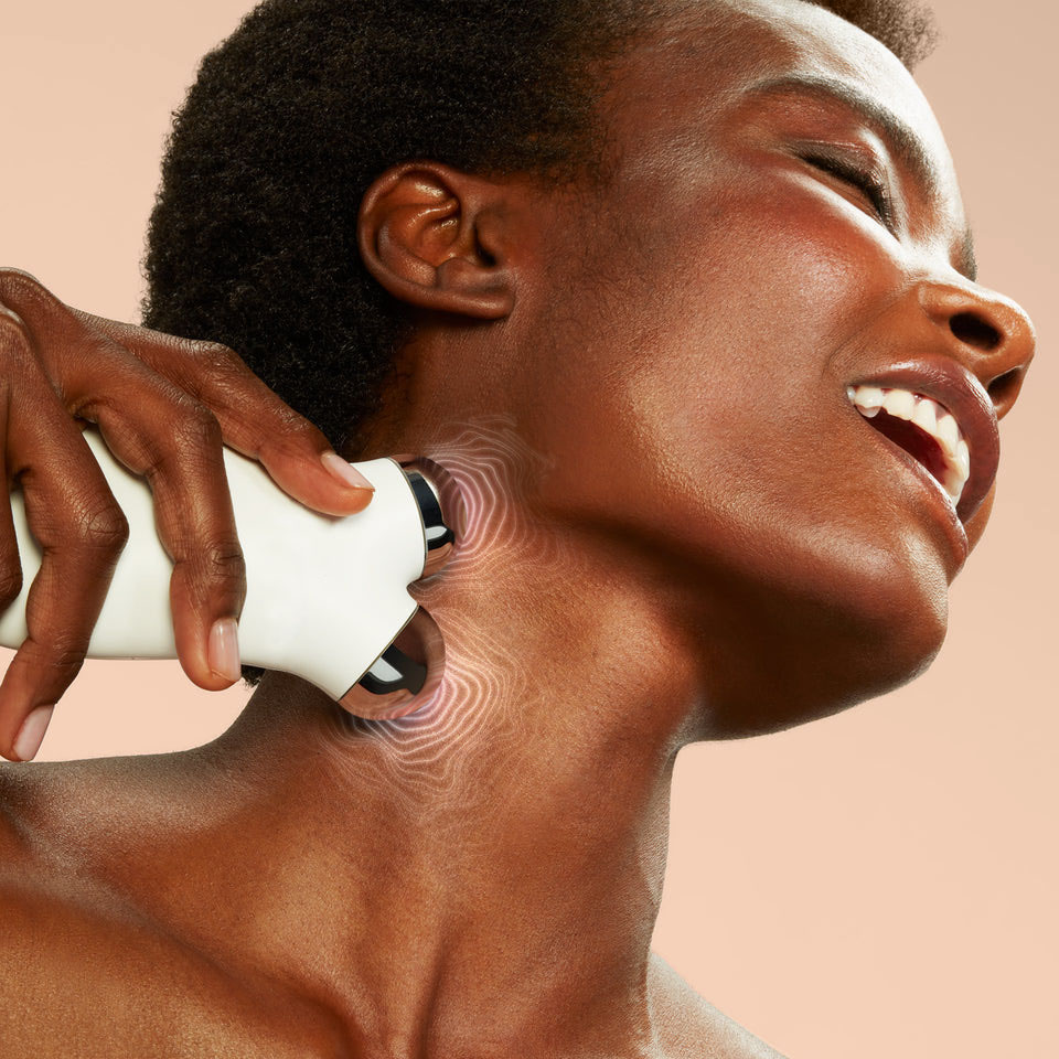 Person using a white handheld device on their neck, smiling.