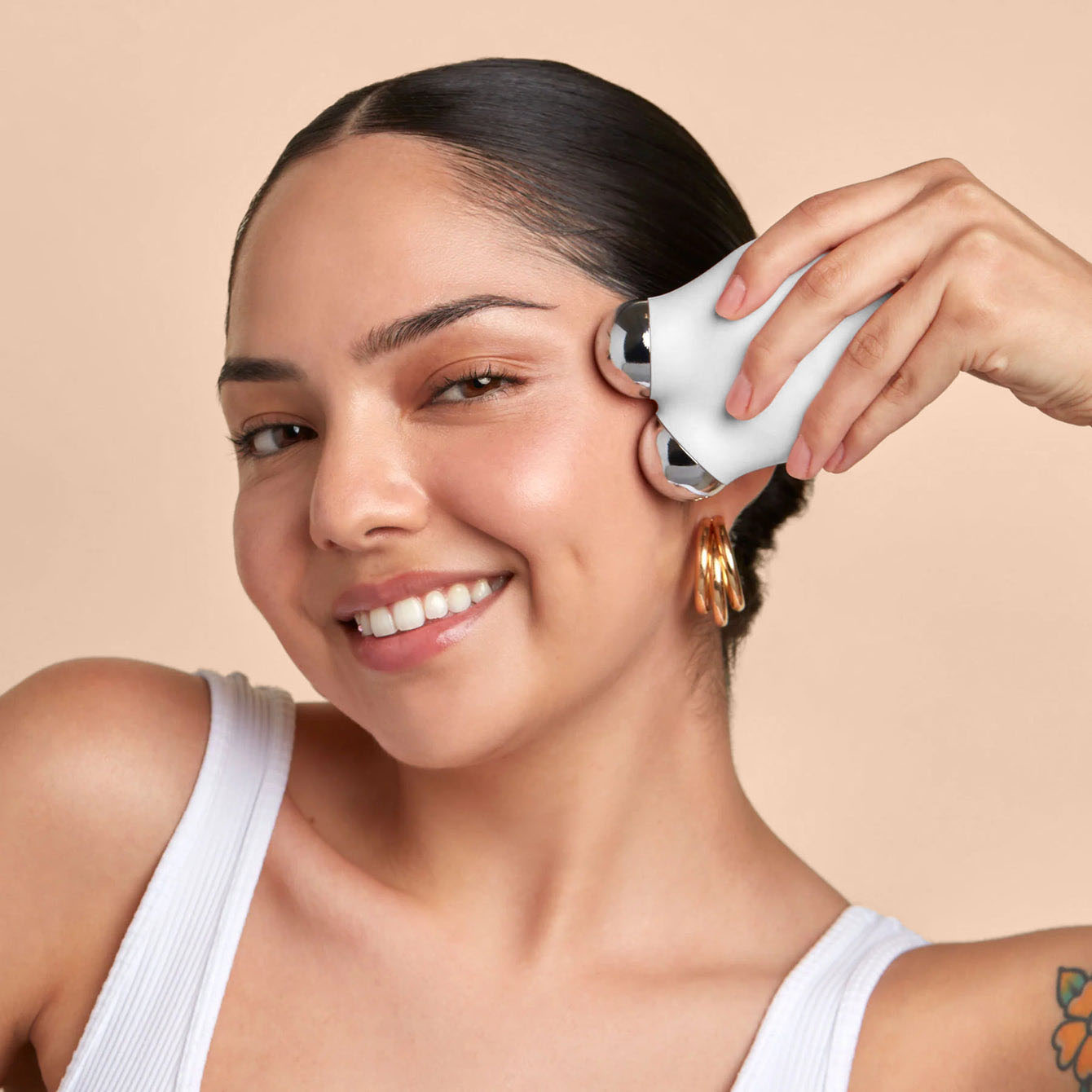 Person using a facial massage device on their cheek, smiling.