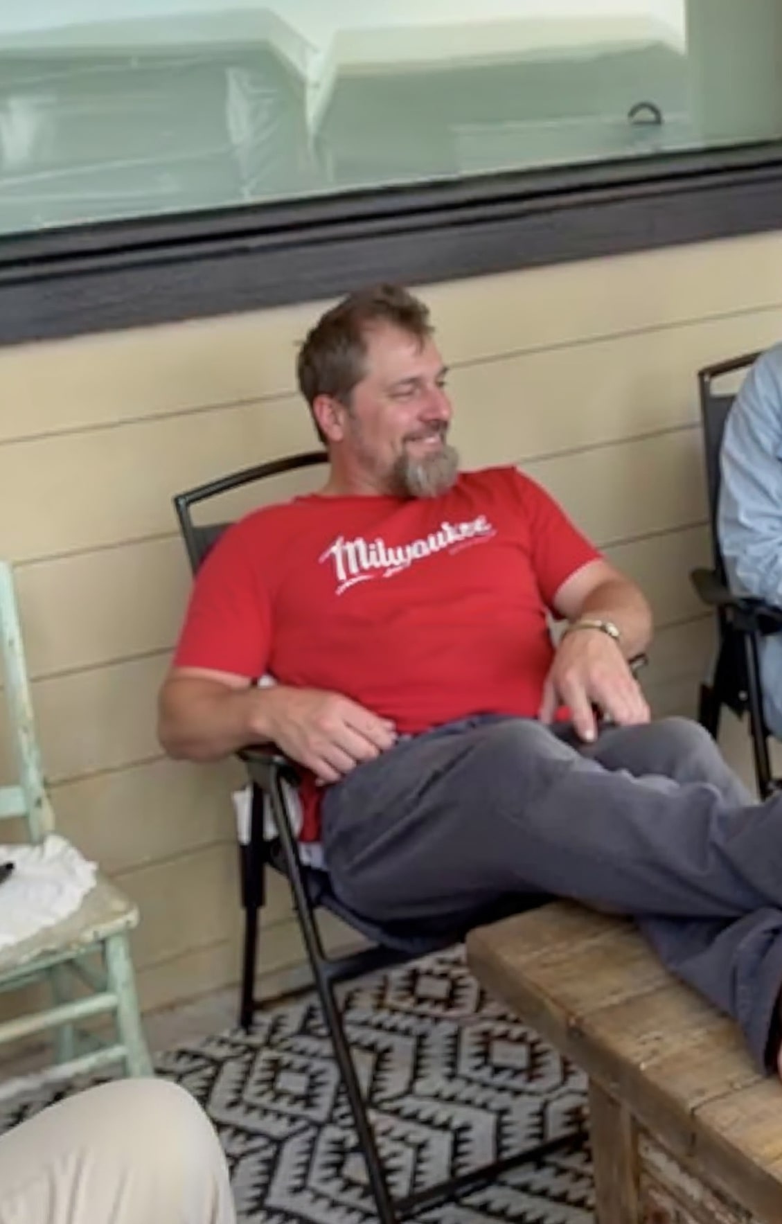 Man in red shirt sitting outdoors, smiling.