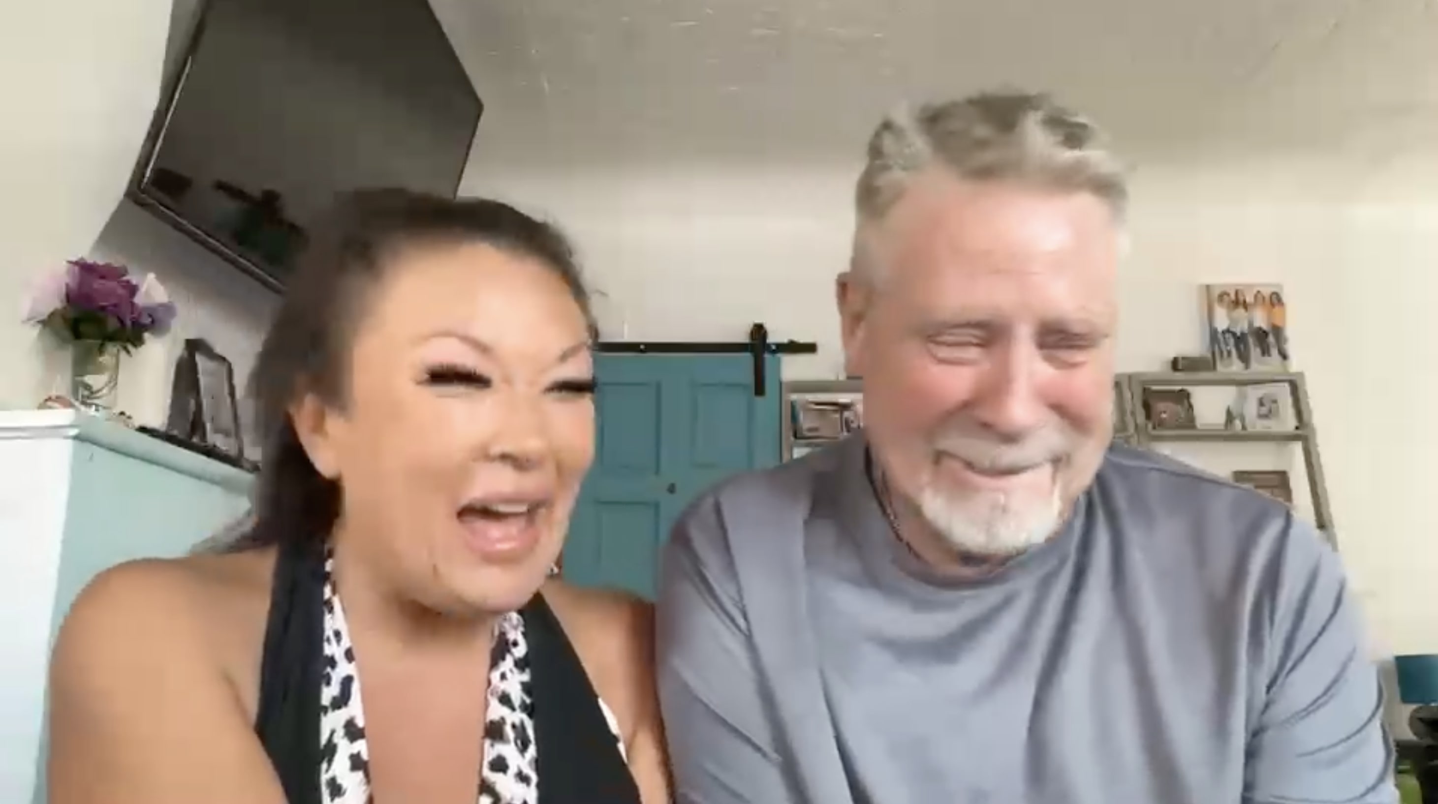 Two people laughing in a room with blue door and wall decorations.