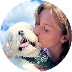 Woman kissing a fluffy dog wearing a bandana on a sunny day.
