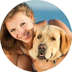 A woman smiling alongside a Labrador Retriever on a sunny day.