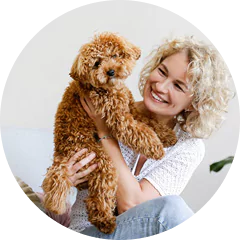 A person smiling while holding a small curly-haired dog.