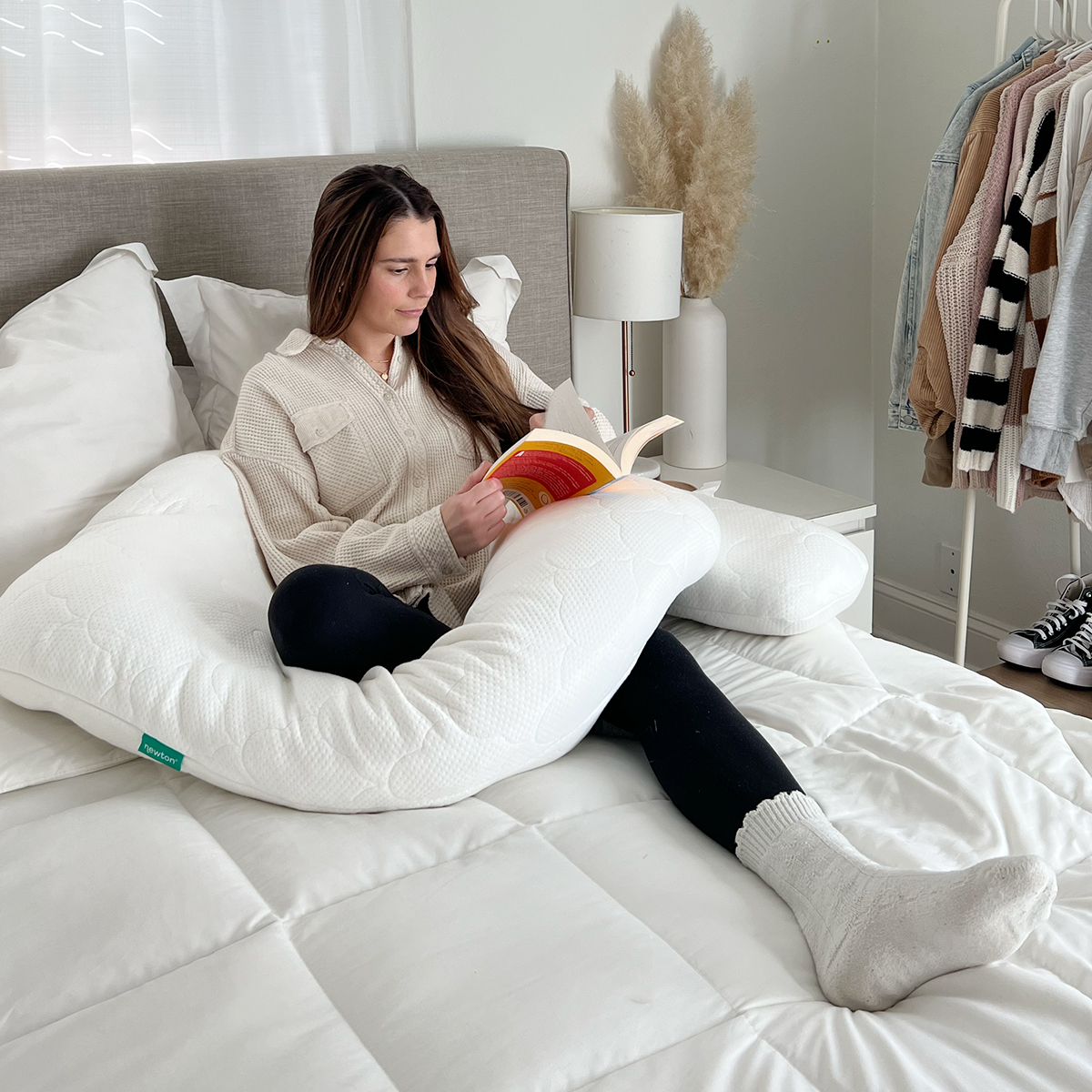 Woman reading a book in bed with The Newton Pillow