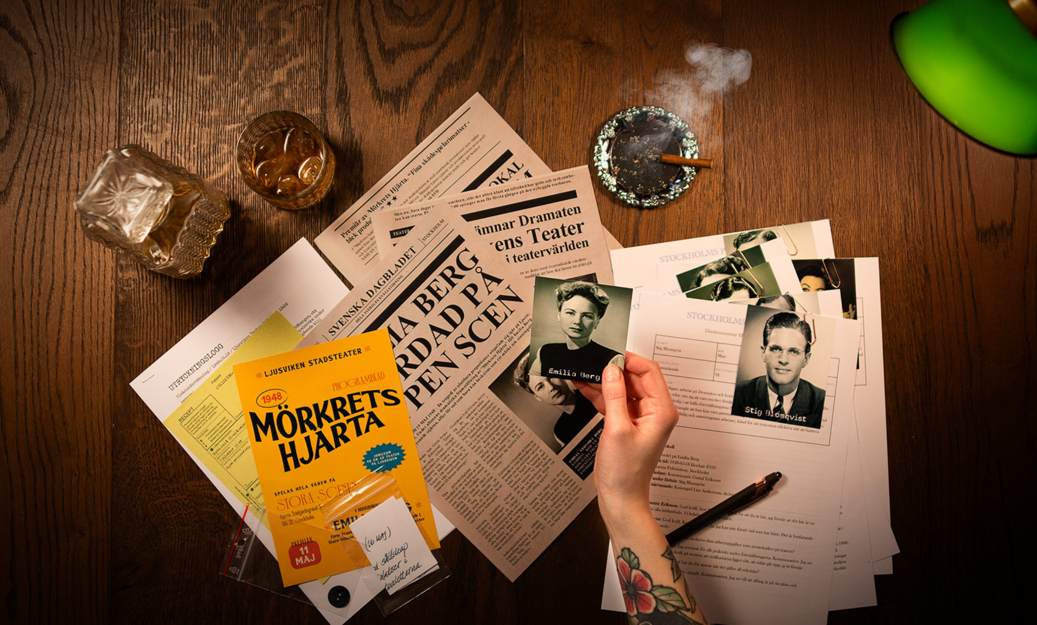 A table with newspapers, photos, a drink, and a hand holding a photograph.