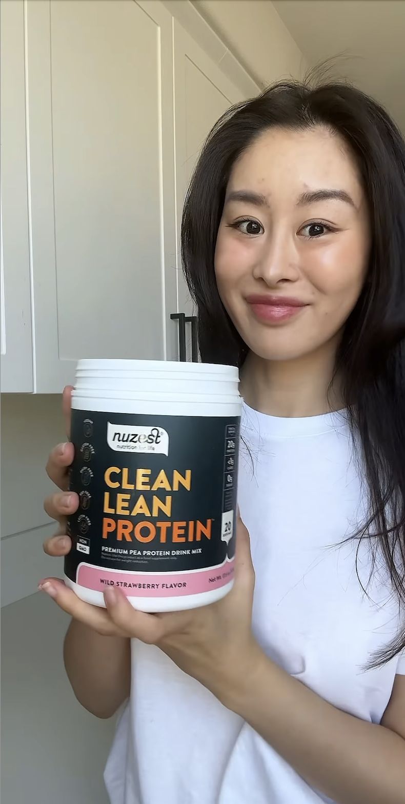 Person holding a container of Clean Lean Protein in a kitchen.