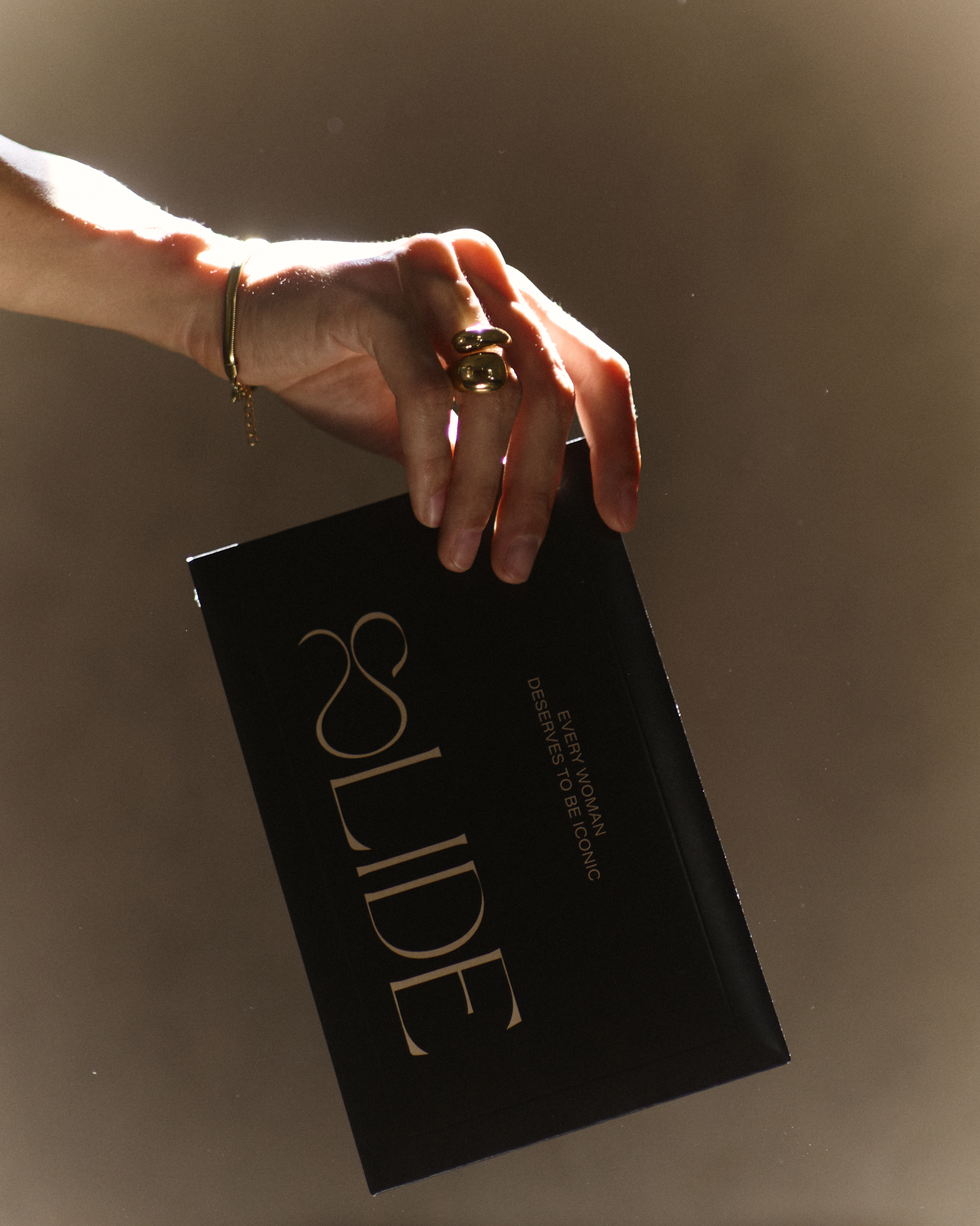Hand holding a black envelope with gold text 'SLIDE.'