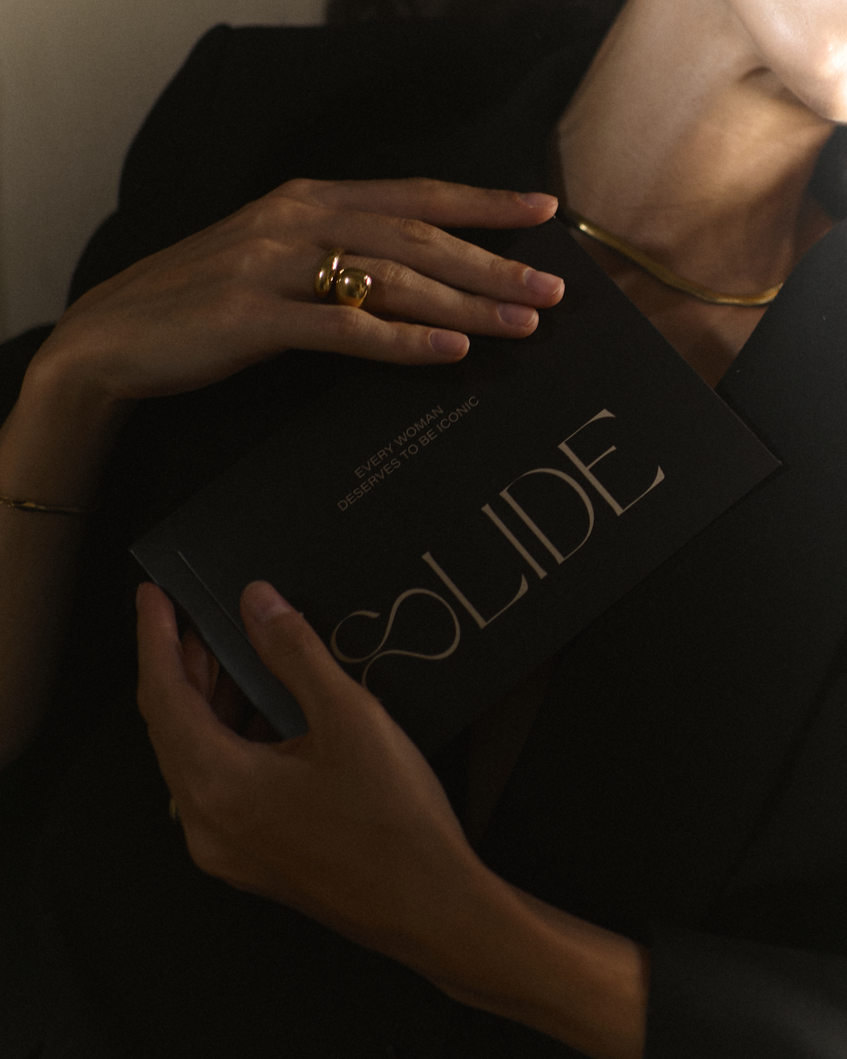 Person holding a black card with gold text, wearing gold jewelry.