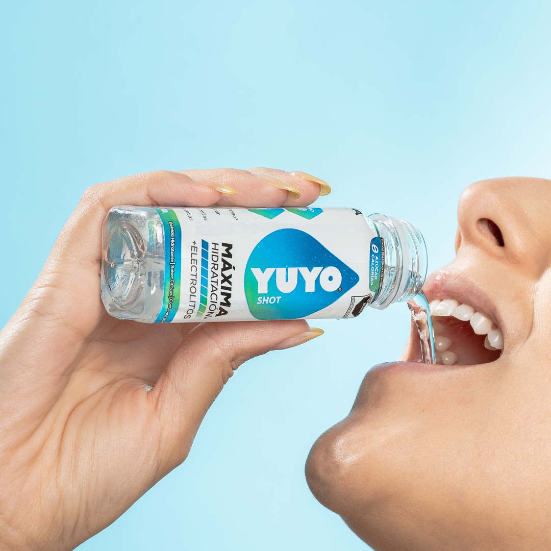 Person drinking from a small bottle labeled 'Yuyo Shot' against a blue background.