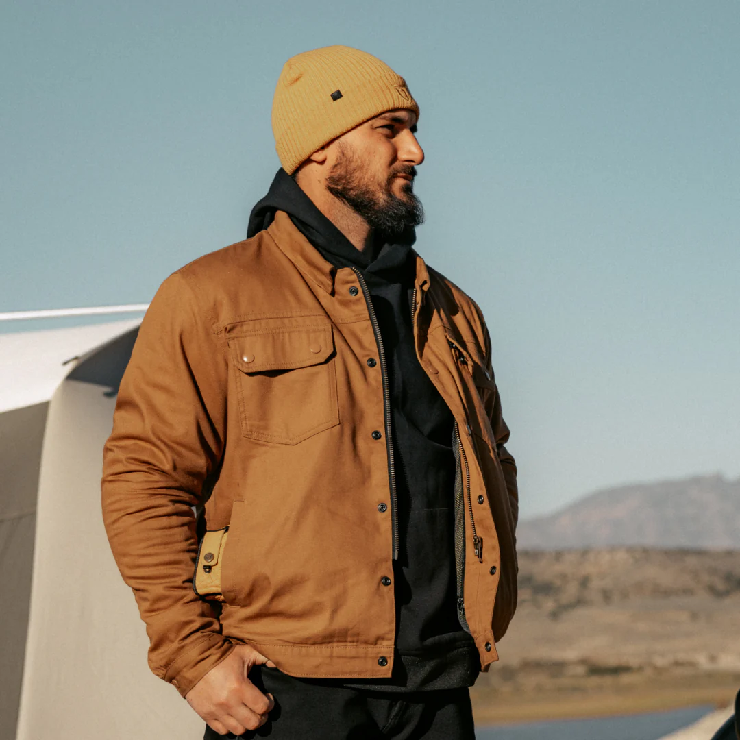 Man in brown jacket and beanie standing outdoors.