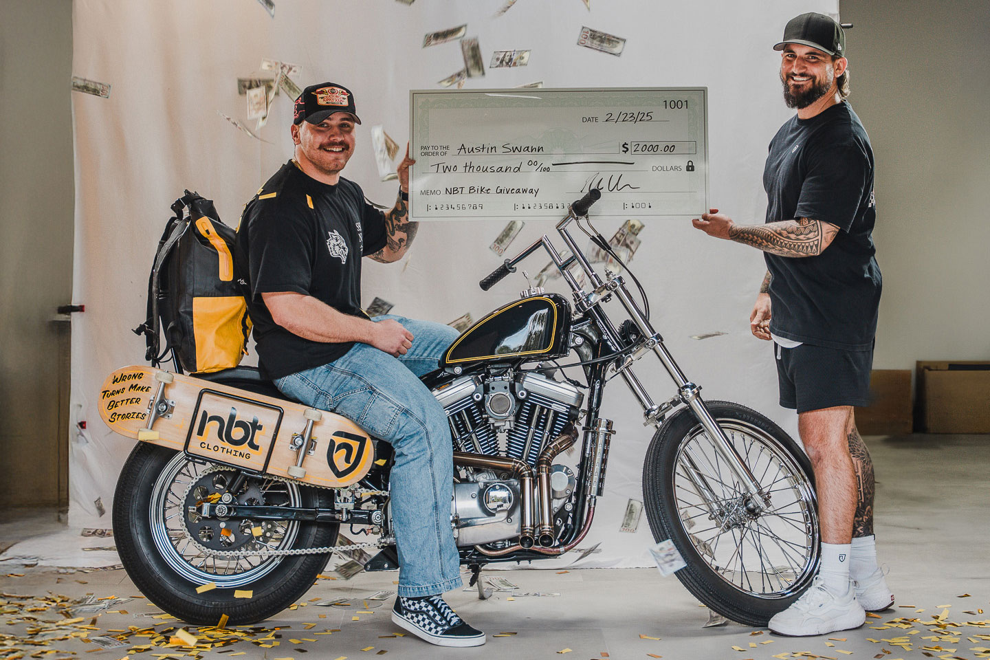 Two men with a motorcycle and a large check, surrounded by falling money.