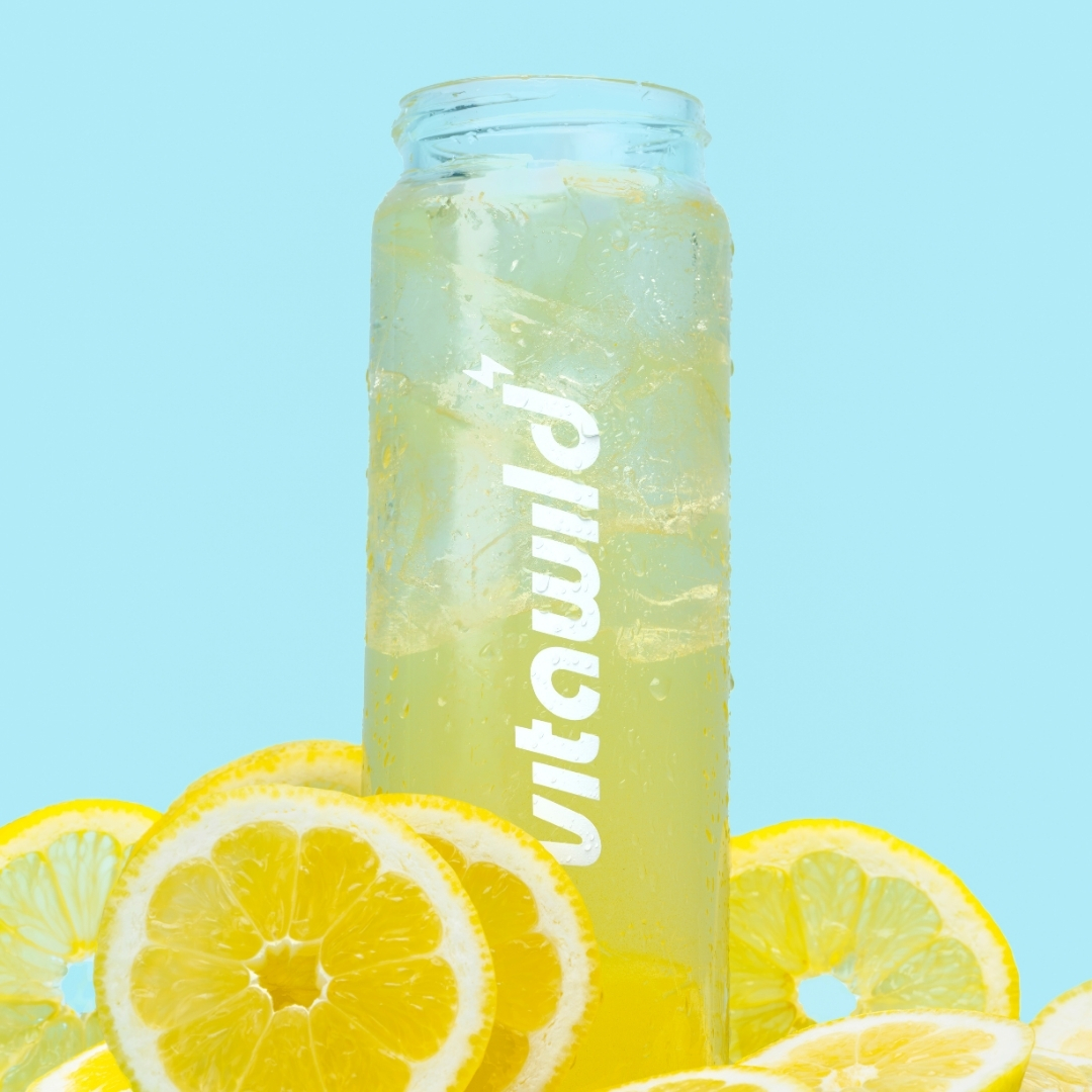 Clear bottle of lemonade with lemon slices against blue background.