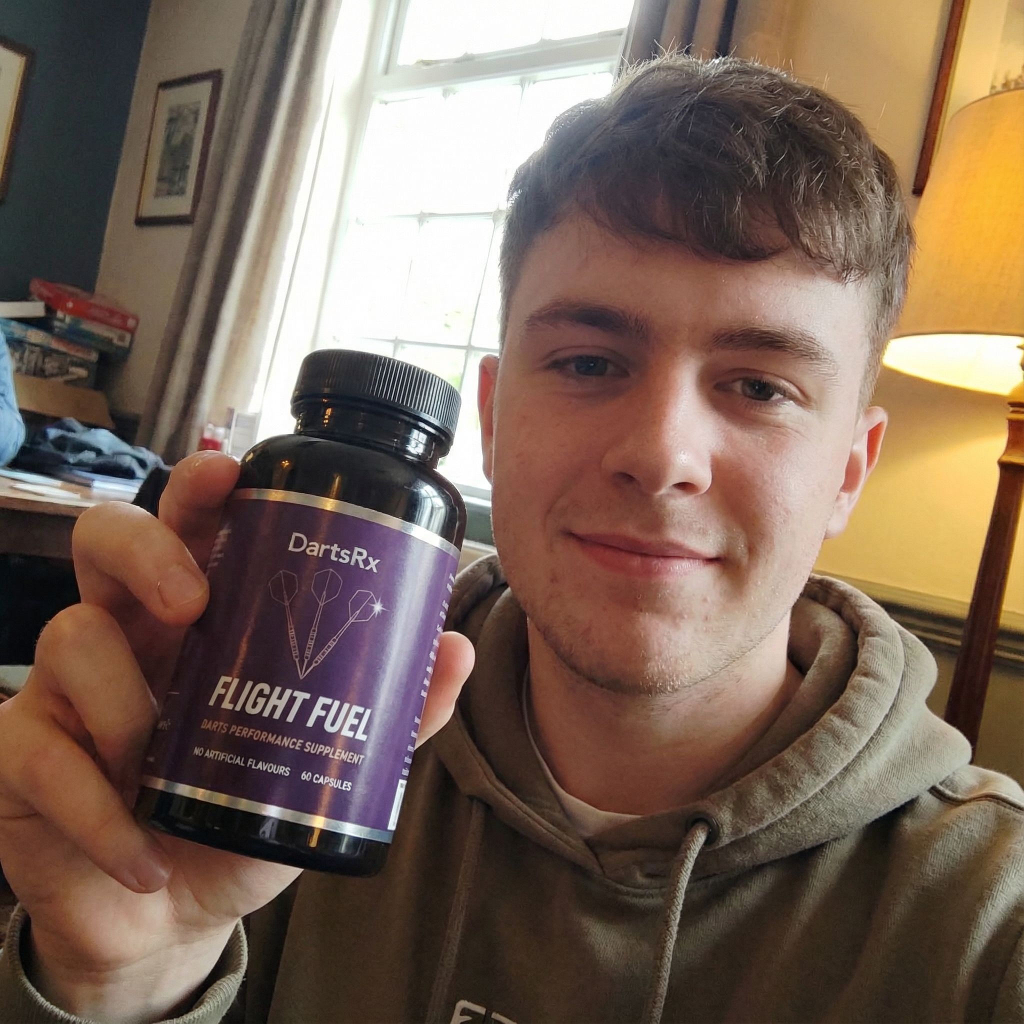 Person holding a bottle of DartsRx Flight Fuel supplement indoors.
