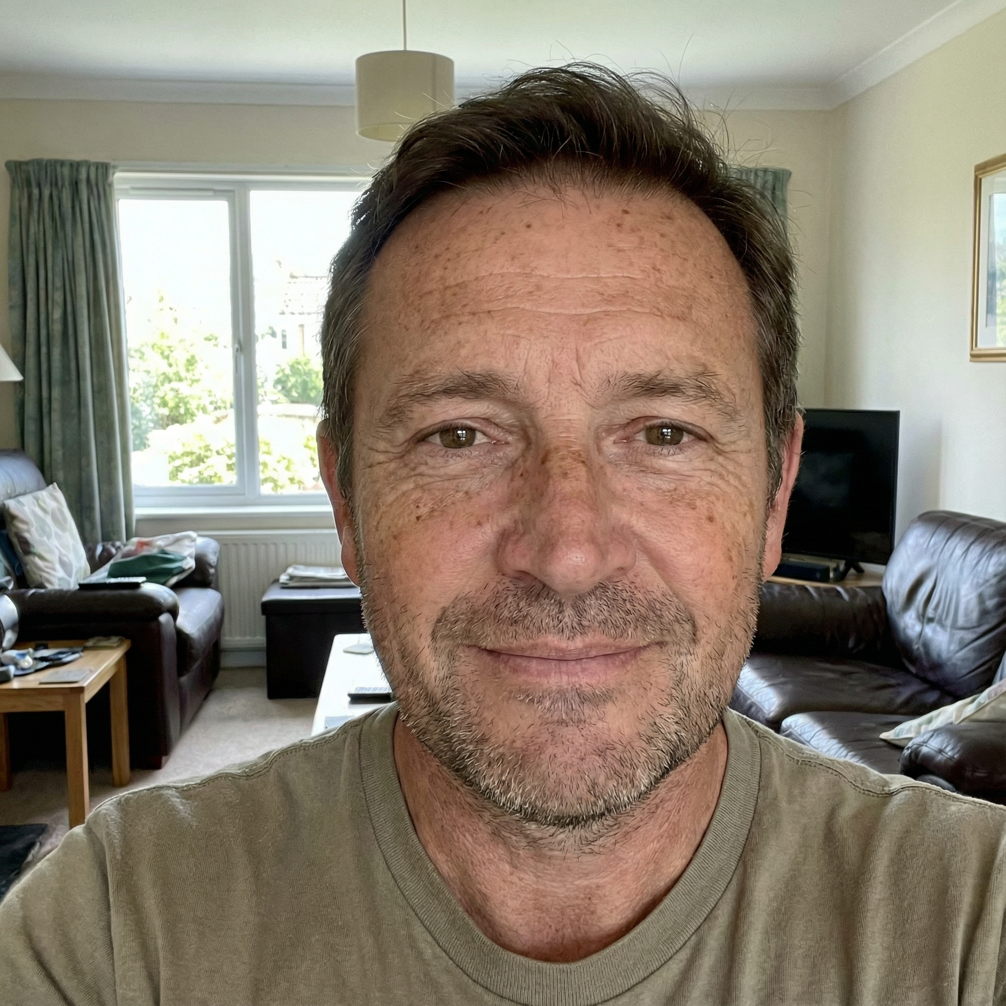 A person smiling indoors with living room furniture in the background.