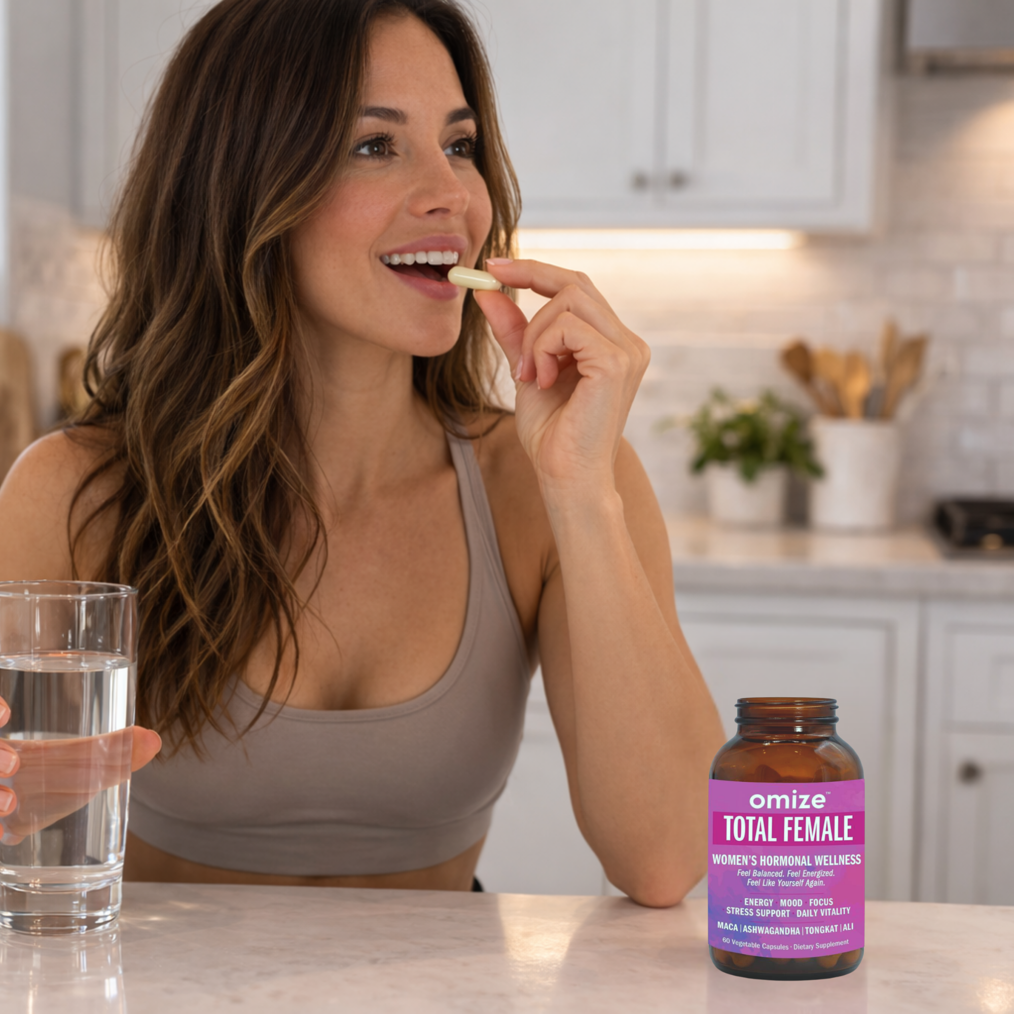 A woman in a sports bra takes a supplement capsule with a glass of water in a kitchen.
